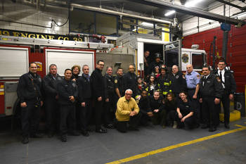 Many people standing in and out of a fire truck and smiling for a commemorative photo